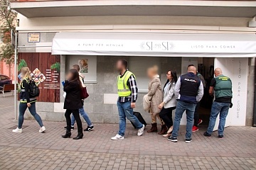Agents de la Guàrdia Civil i de la policia espanyola sortint d'uns dels establiments escorcollats amb una dona detinguda en l'operació feta a Torredembarra